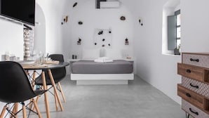A modern bedroom with a bed, bedside tables, a TV, and a dining area with chairs and a table. - Noelia Suites - Prive by ΜΡS (OIA)