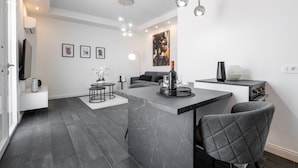 Et moderne køkken med mørke fliser, en central ø, hængende lamper og et spiseområde med en sofa og stole.