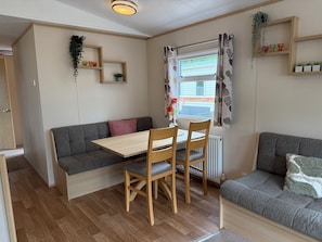 A cozy room with a wooden dining table, two chairs, a grey sofa, and a window with curtains.