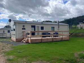 A mobile home with a deck, a grill, and a nameplate.