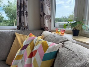A sofa with colorful pillows, a window with curtains, and a potted plant on a windowsill.
