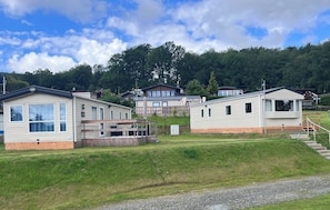 A row of mobile homes with a grassy area in front, wooden decks, and a hill with trees in the background.