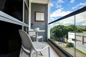 Ein Balkon mit zwei Stühlen und einem Tisch, ein gerahmtes Zertifikat an der Wand und Blick auf Grünflächen und Gebäude.