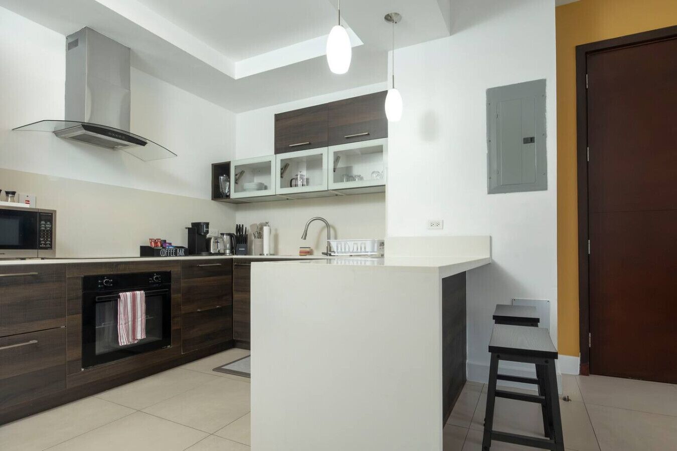 A modern kitchen with a central island, dark wood cabinetry, a stainless steel range hood, and pendant lighting.