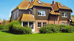 Uma casa de dois andares com telhado inclinado, varanda coberta e jardim bem cuidado.