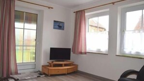 Quarto com televisão sobre um suporte de madeira, janela com cortinas e um quadro na parede.
