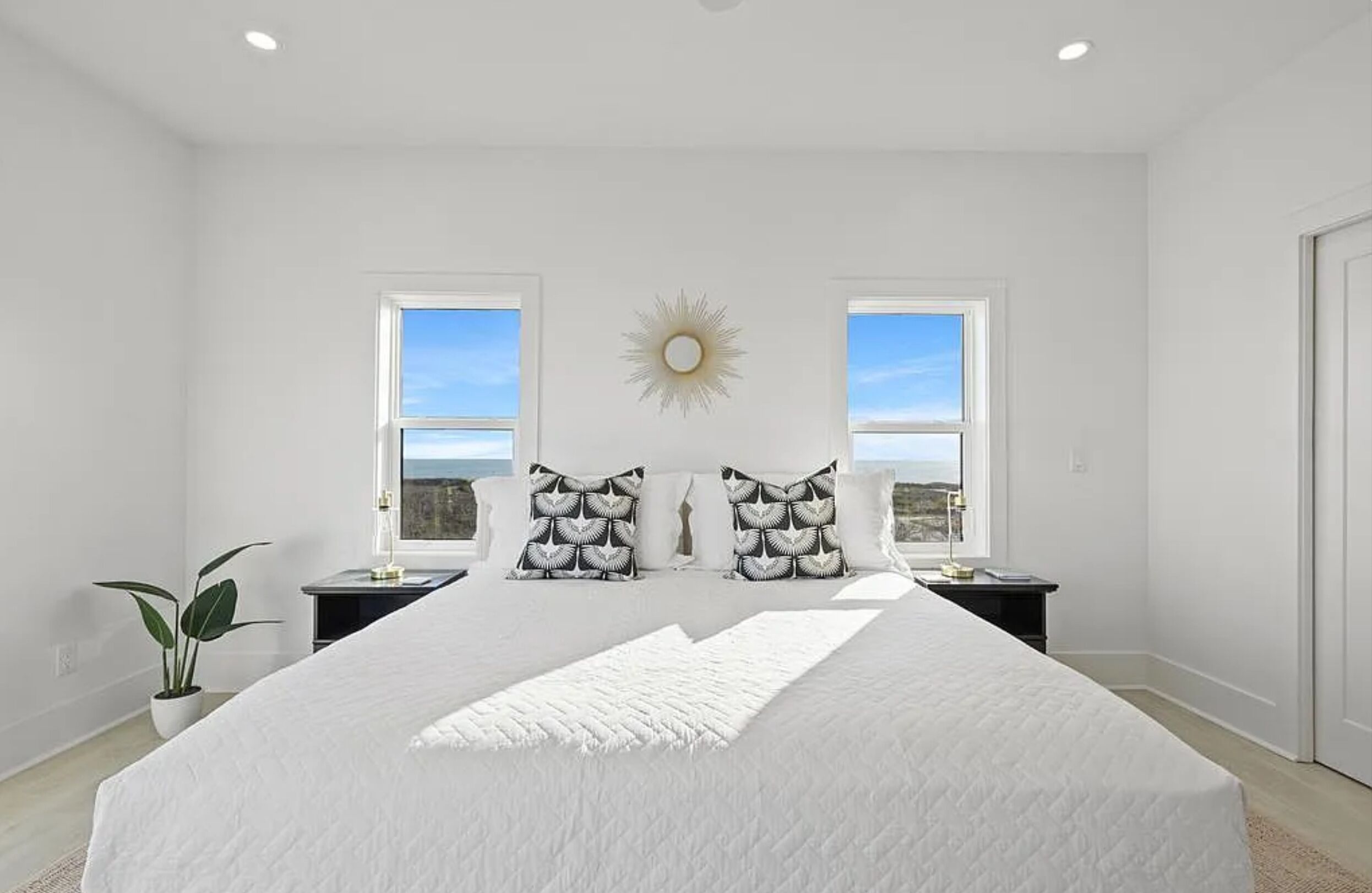 A bedroom with a large bed, two nightstands, a potted plant, and a sunburst wall decoration.