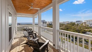 Un balcon abrité avec un plancher en bois, des balustrades blanches et un ventilateur de plafond.