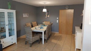 Un coin repas avec une table et des chaises, un meuble avec des portes en verre, une horloge au mur et une porte.