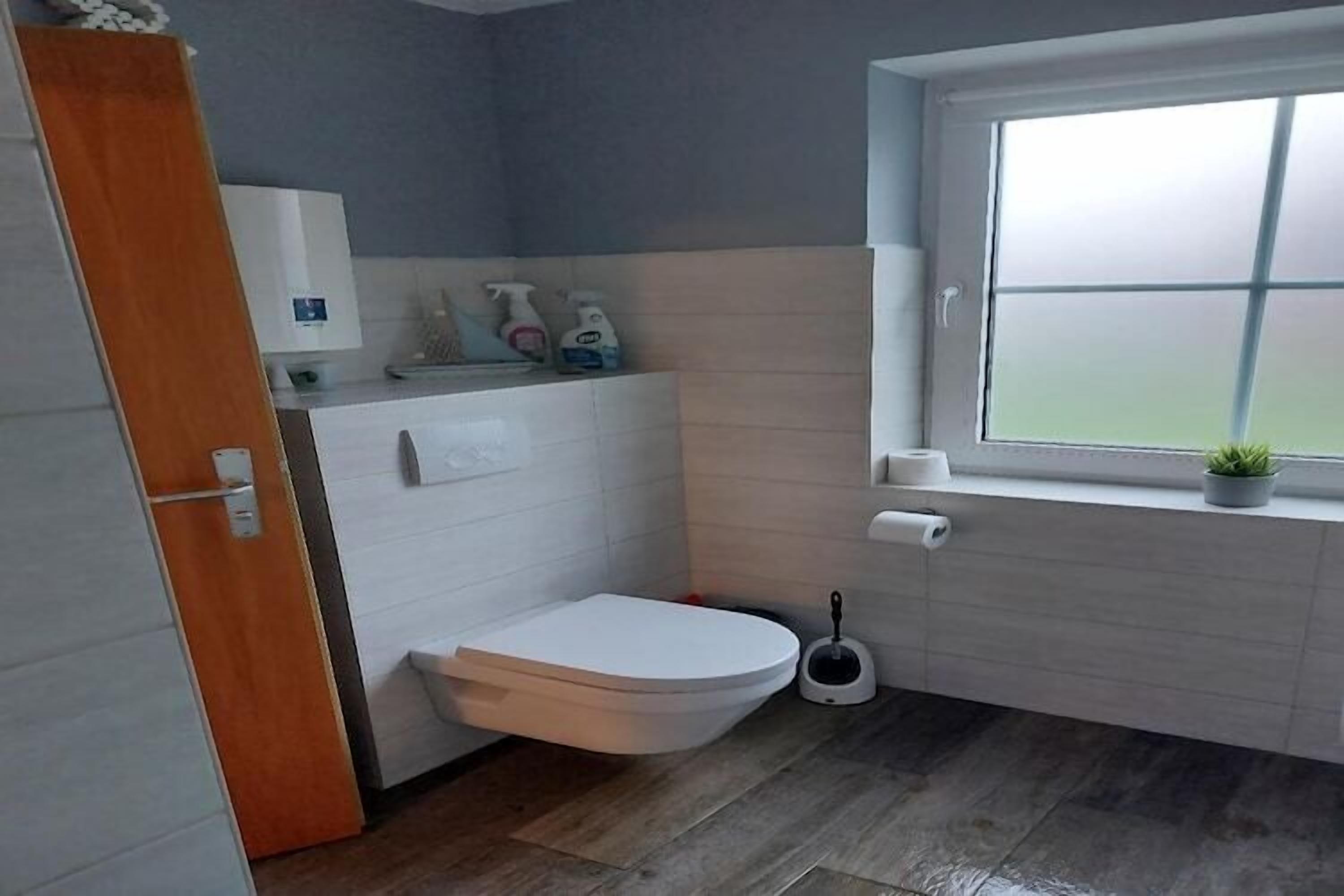 Et badeværelse med toilet, bidet, et vindue og en lille potteplante.