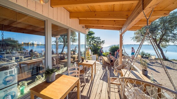 Een houten terras buiten, met tafels en stoelen, met uitzicht op een wateroppervlak.