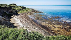 Een kustlandschap met een rotsachtige kustlijn, helderblauw water en land in de verte.