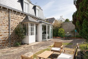 A stone building with a glass conservatory, outdoor seating, and a garden area. - Pomme de Pins - À 1km de la plage (Pléneuf-Val-André)