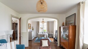 Ein Wohnzimmer mit einem blauen Sofa, einem braunen Sessel, einer Holzkommode und einem Essbereich mit Tisch und Stühlen.