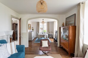 A living room with a blue sofa, a brown armchair, a wooden cabinet, and a dining area with a table and chairs. - Pomme de Pins - À 1km de la plage (Pléneuf-Val-André)
