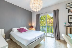A bedroom with a bed, bedside table, lamp, and a view of the outdoors. - Villa Joana - piscine, grand jardin, 4 chambres (Arbonne)