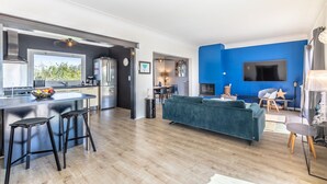 Une cuisine moderne dotée d’un grand îlot central, un coin repas avec un canapé bleu et un salon avec une télévision et une cheminée.