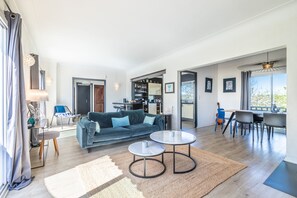 Un salon moderne comprenant un canapé, deux tables rondes, une table basse et un coin repas avec des chaises.