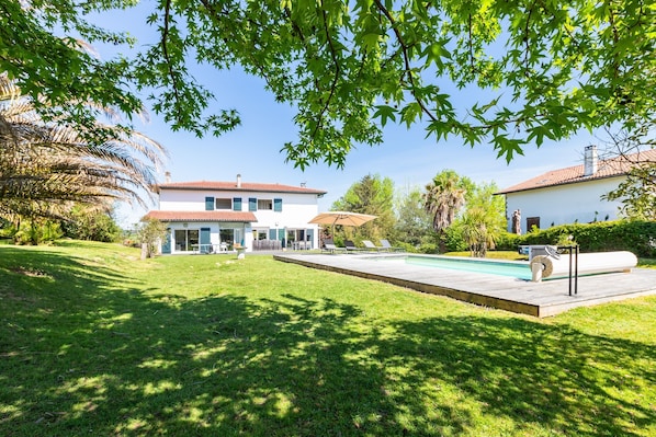 Une maison à deux étages avec une piscine, entourée d’une pelouse bien entretenue et d’arbres.