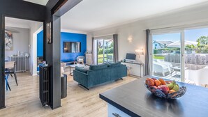 Un salon moderne avec un mur d’accent bleu, un canapé foncé, un coin repas avec une table et une grande fenêtre donnant sur l’extérieur.