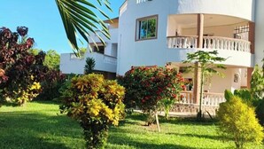 A multi-story building with balconies, surrounded by well-maintained gardens and various plants. - cosy by-beach retreat!Warm private escape with private pool (Kwale County)