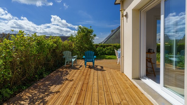 A wooden deck with two chairs, a glass door leading to a room, and a clear sky. - Fenêtre sur mer - À 400m de la plage (Saint-Nic)