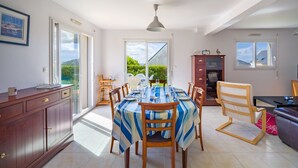 A dining area with a table set for four, a wooden cabinet, and a view of the outdoors. - Fenêtre sur mer - À 400m de la plage (Saint-Nic)