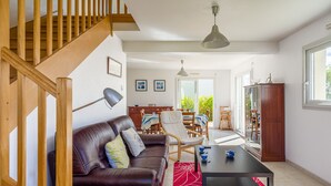 A modern living room with a wooden staircase, a leather sofa, a dining area, and a large window. - Fenêtre sur mer - À 400m de la plage (Saint-Nic)