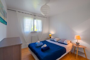 Ein Schlafzimmer mit einem Bett, einem Nachttisch mit Lampe, einem Heizkörper und einem Fenster mit Vorhängen.