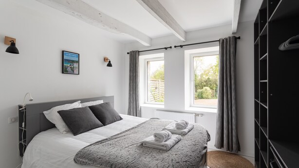 Ein Schlafzimmer mit einem Bett, einem Fenster mit Vorhängen, einer Wandlampe und einem gerahmten Bild.