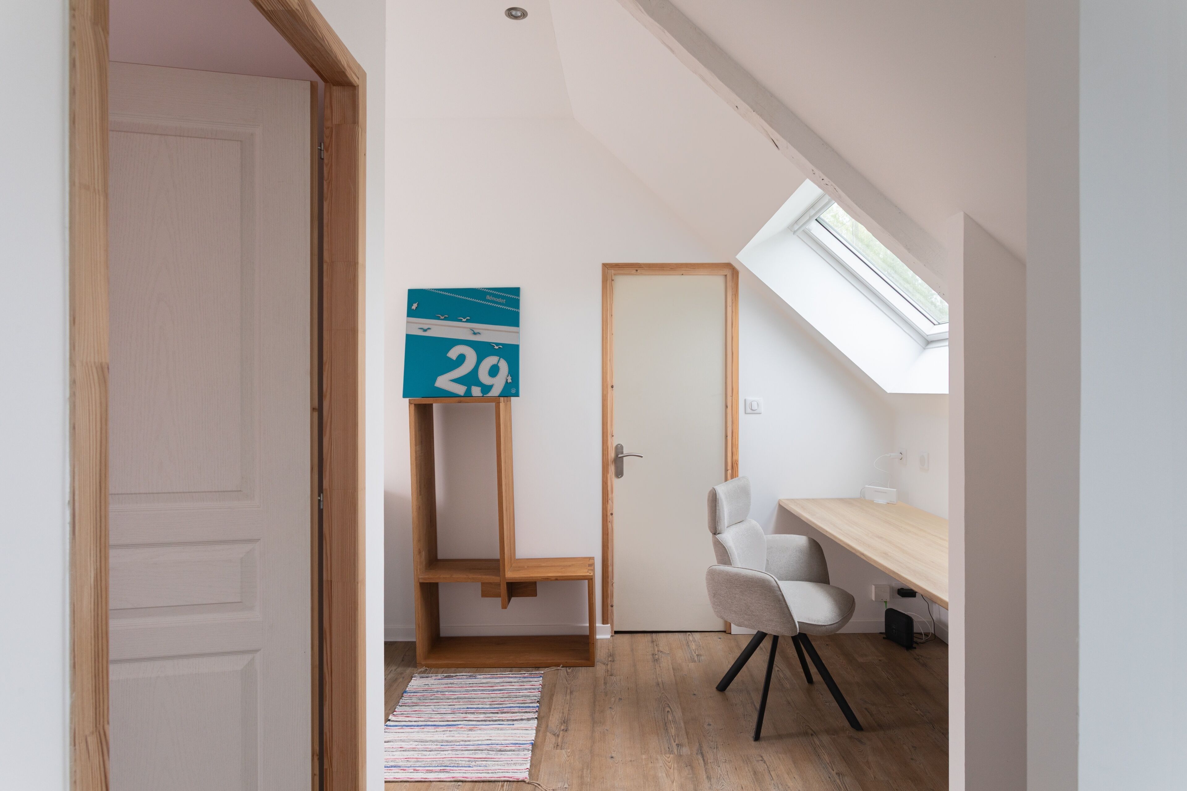 Une pièce comprenant un bureau, une chaise, une lucarne et une porte.