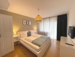 A bedroom with a bed, bedside tables, a TV, and a hanging light fixture. - City apartment SB Am Homburg (ground floor, Ap 0) (Saarbrücken)