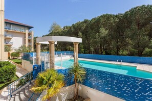 Ein Poolbereich mit einer Pergola, Palmen und einem Gebäude mit Balkonen.