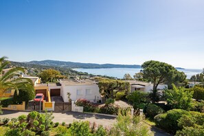 Zona residencial con casas, un auto rojo y vista al mar.