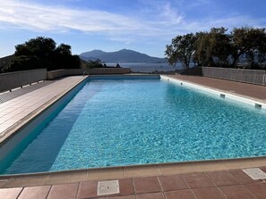 A rectangular swimming pool with clear blue water, surrounded by a tiled deck and a metal railing.