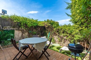 A patio with a table and chairs, a barbecue grill, and a lush garden. - Terra Bella 2 - Vue Mer (Grosseto-Prugna)