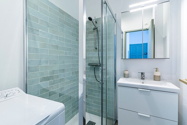 A bathroom with a glass shower enclosure, a white sink, and a mirror above the sink.