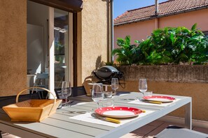 An outdoor dining area with a table set for two, a grill, and lush greenery in the background. - MCC House - Avec terrasse privée (Quillan)