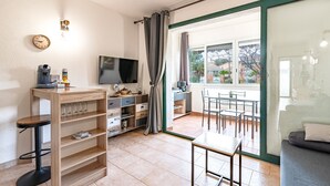 A modern living space with a TV, wooden furniture, a dining area, and a view through a glass door. - Casa di Bravone - À 150m de la plage (Linguizzetta)