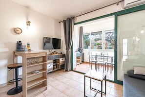 Un espacio habitable moderno con televisor, muebles de madera, una zona de comedor y vistas a través de un ventanal.