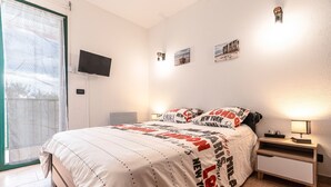 A bedroom with a bed, a TV, a nightstand, and a window with curtains. - Casa di Bravone - À 150m de la plage (Linguizzetta)