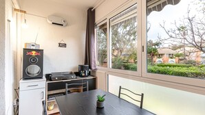 A compact room with a dining table, a small potted plant, a coffee machine, a speaker, and a window with a view of greenery and buildings. - Casa di Bravone - À 150m de la plage (Linguizzetta)