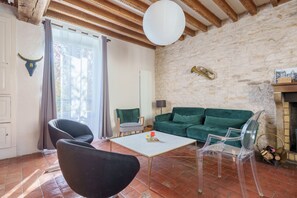 Ein rustikales Wohnzimmer mit Steinwand, Holzbalken, einem grünen Sofa, einem weißen Couchtisch und einem klaren Stuhl.
