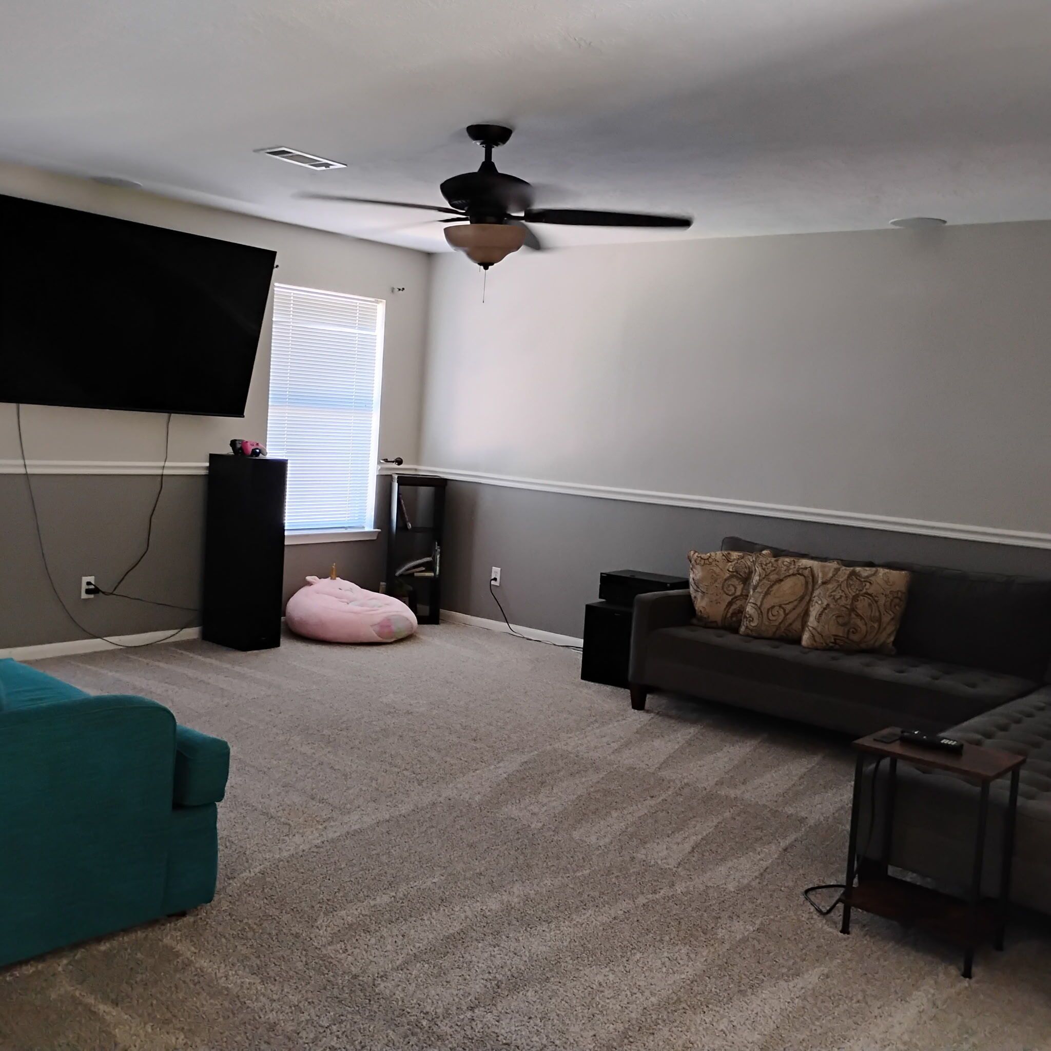 A living room with a ceiling fan, a flat-screen TV, a sofa, a bean bag, and a coffee table.