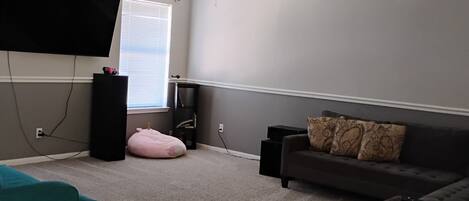 A living room with a ceiling fan, a flat-screen TV, a sofa, a bean bag, and a coffee table.