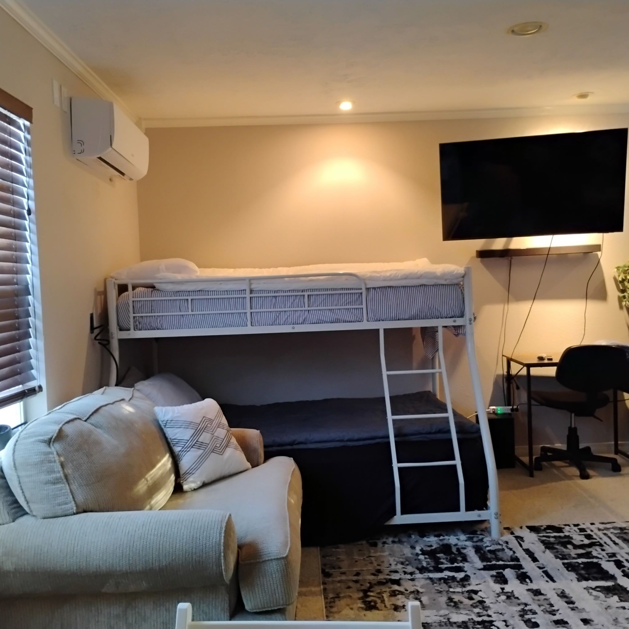 Un lit superposé avec un bureau et une chaise, un canapé, une télévision et un climatiseur.