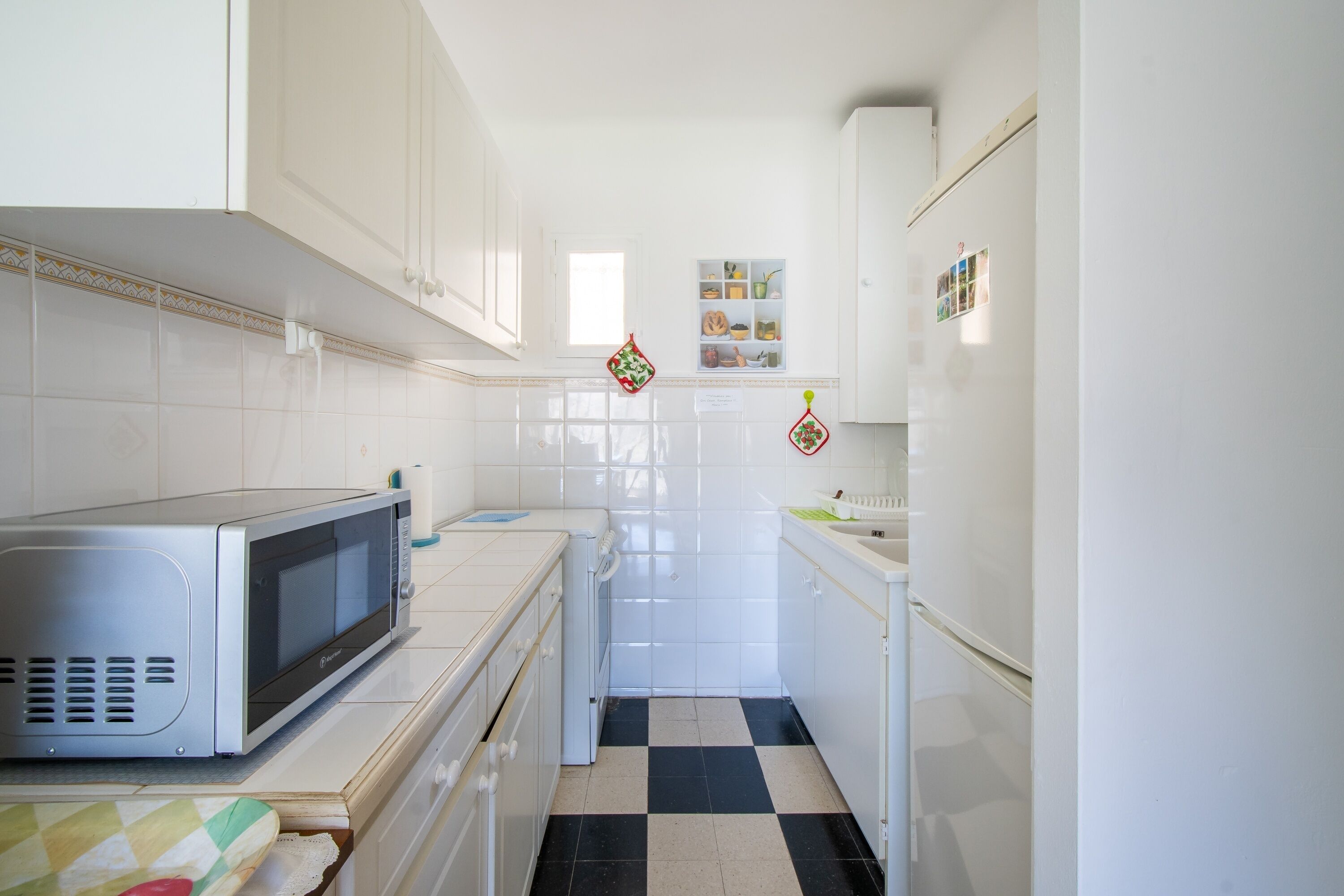 A kitchen with white cabinets, a microwave, a sink, and a checkered floor.
