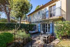 Ein Haus mit Balkon, einer Terrasse mit Gartenmöbeln und einem gepflasterten Weg.
