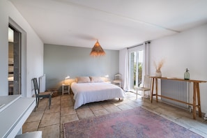 Una camera da letto con un letto, comodini, una sedia, una lampada a sospensione e vista dalla finestra.