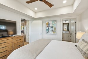 Quarto com cama, televisão, guarda-roupa, quadro, espelho e ventoinha no teto.